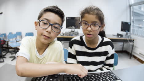 Schoolkids sitting at table and typing on computer keyboard