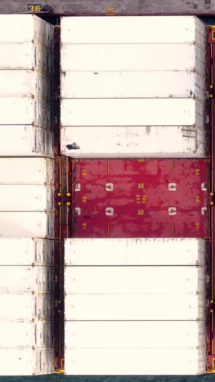A container ship is docked at a busy cargo terminal. Shipping containers are stacked and organized for global shipping. This process supports international trade and freight transportation.