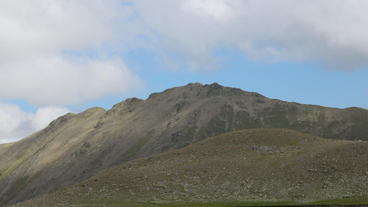 Inquadratura ampia di una cresta montuosa rocciosa e verdi pendii alpini sotto un cielo azzurro nuvoloso a Dombay, Caucaso, Russia, paesaggio estivo naturale per temi di viaggio e natura.