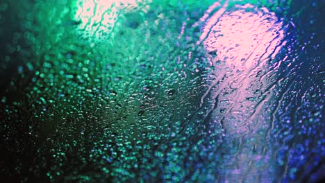 close up of rain water drops on car window glass with blurred traffic lights background at night.