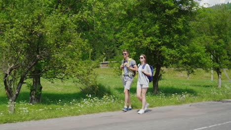A-Young-Tourist-Couple-Walks-Along-The-Road-To-Beautiful-Mountains-Covered-With-Forest-Active-Way-Of