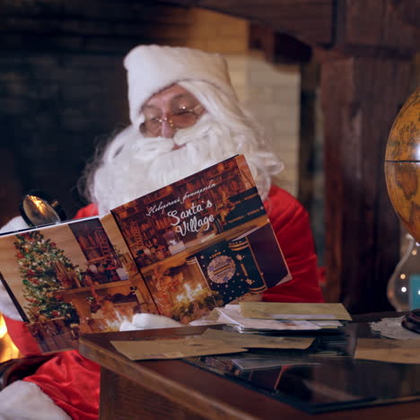 santa reading magic book. real santa claus looking into a christmas book on the fireplace background. round globe on the table. christmas spirit concept.