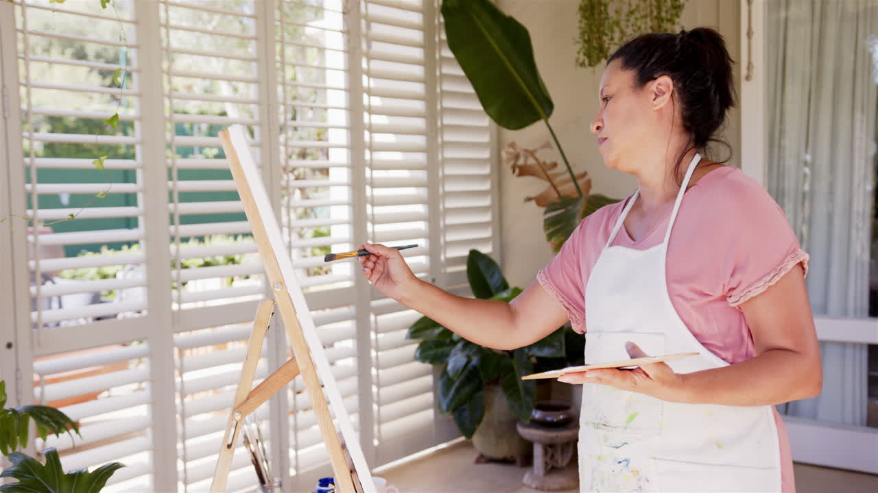 Painting on canvas, woman holding palette and brush in bright room