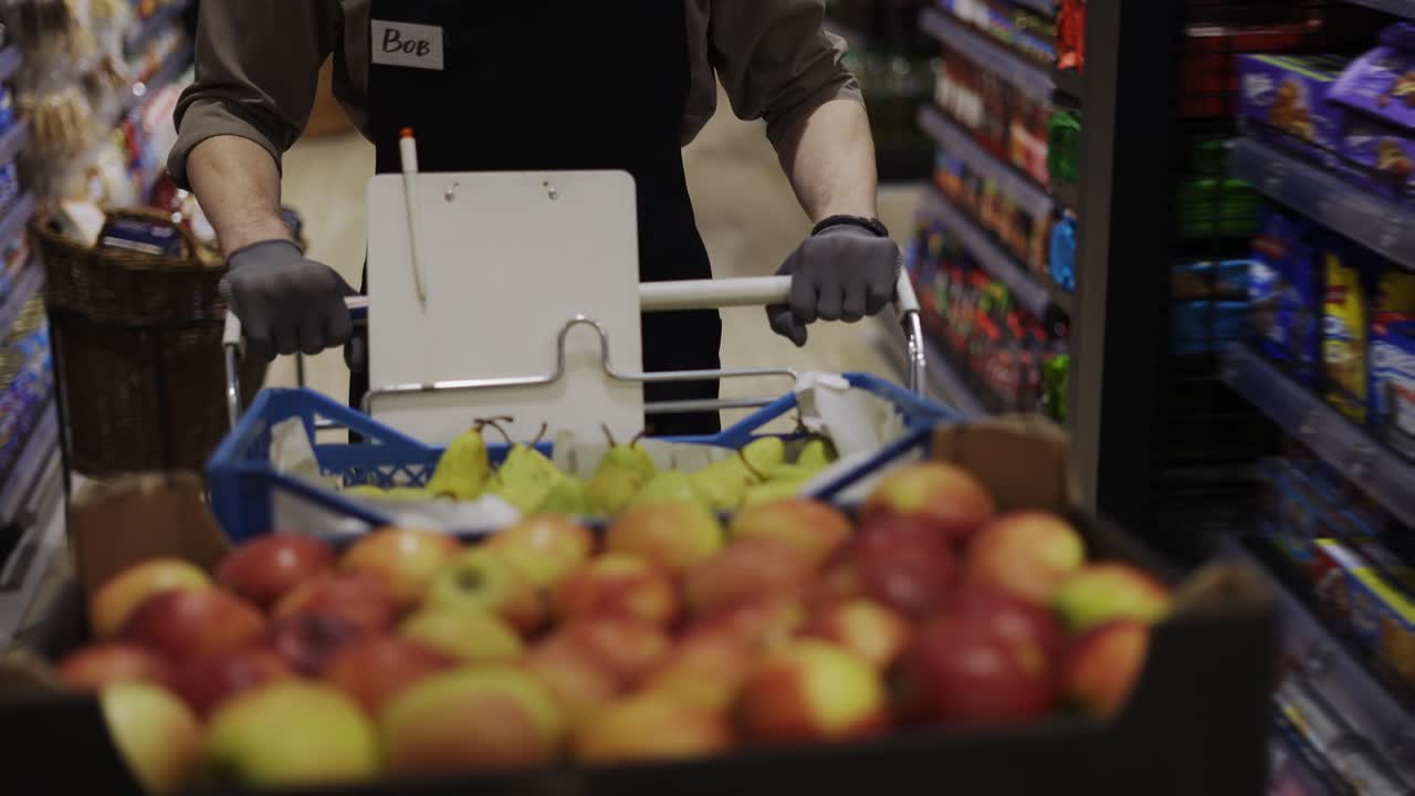 특별한 유니폼을 입은 남자가 식료품 가게의 카트에 과일을 들고 있다.