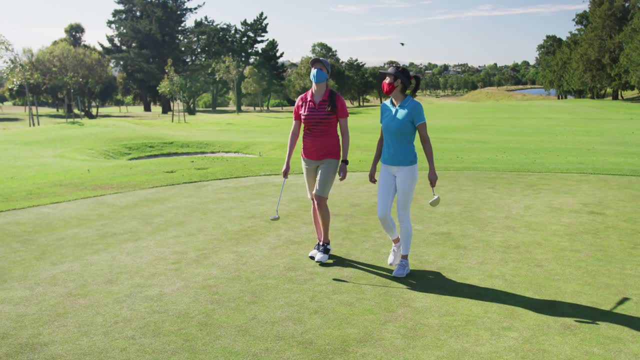 Due donne caucasiche che giocano a golf, indossando mascherine e camminando insieme.