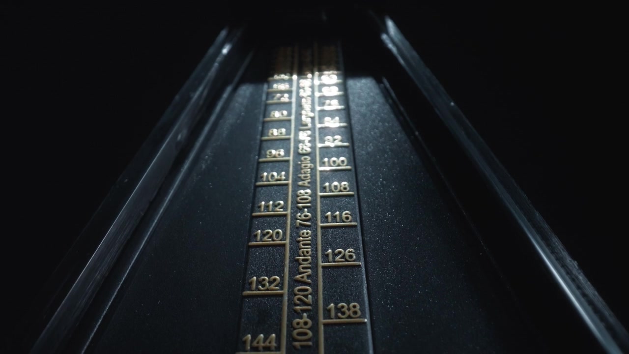 Dolly shot of a vintage black metronome swinging back and forth
