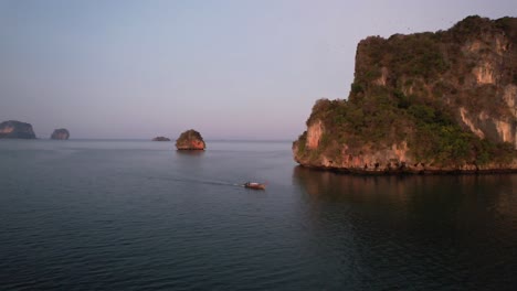 Große-Luftaufnahme-Eines-Einzelnen-Thailändischen-Longtail-Bootes,-Das-Während-Des-Sonnenaufgangs-In-Der-Andamanensee-In-Der-Nähe-Der-Großen-Kalkberge-Des-Railay-Beach-In-Krabi,-Thailand,-Fährt