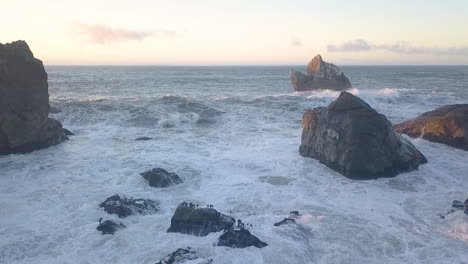 aerial drone of waves crashing against rocks and birds flying over water at sue-meg state park