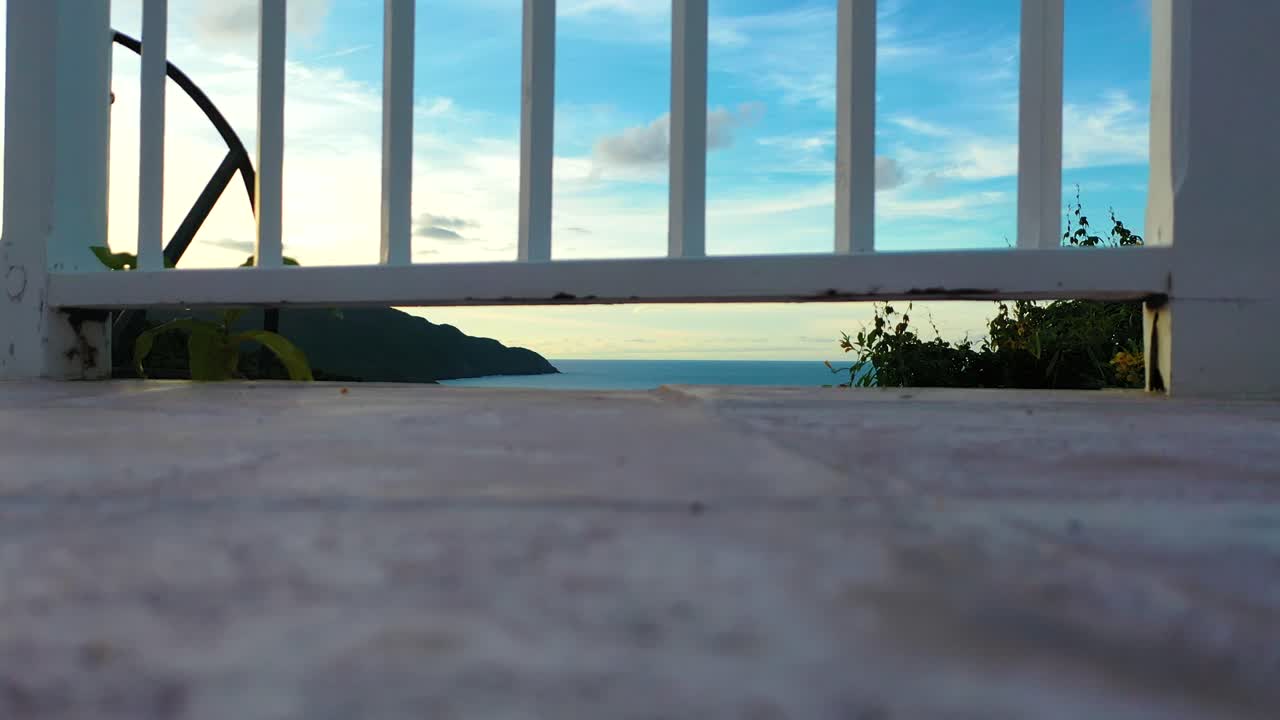 Close-up of a white wooden fence overlooking the ocean, with lush green forest beyond, creating a serene coastal scene framed by natural beauty and gentle seaside charm