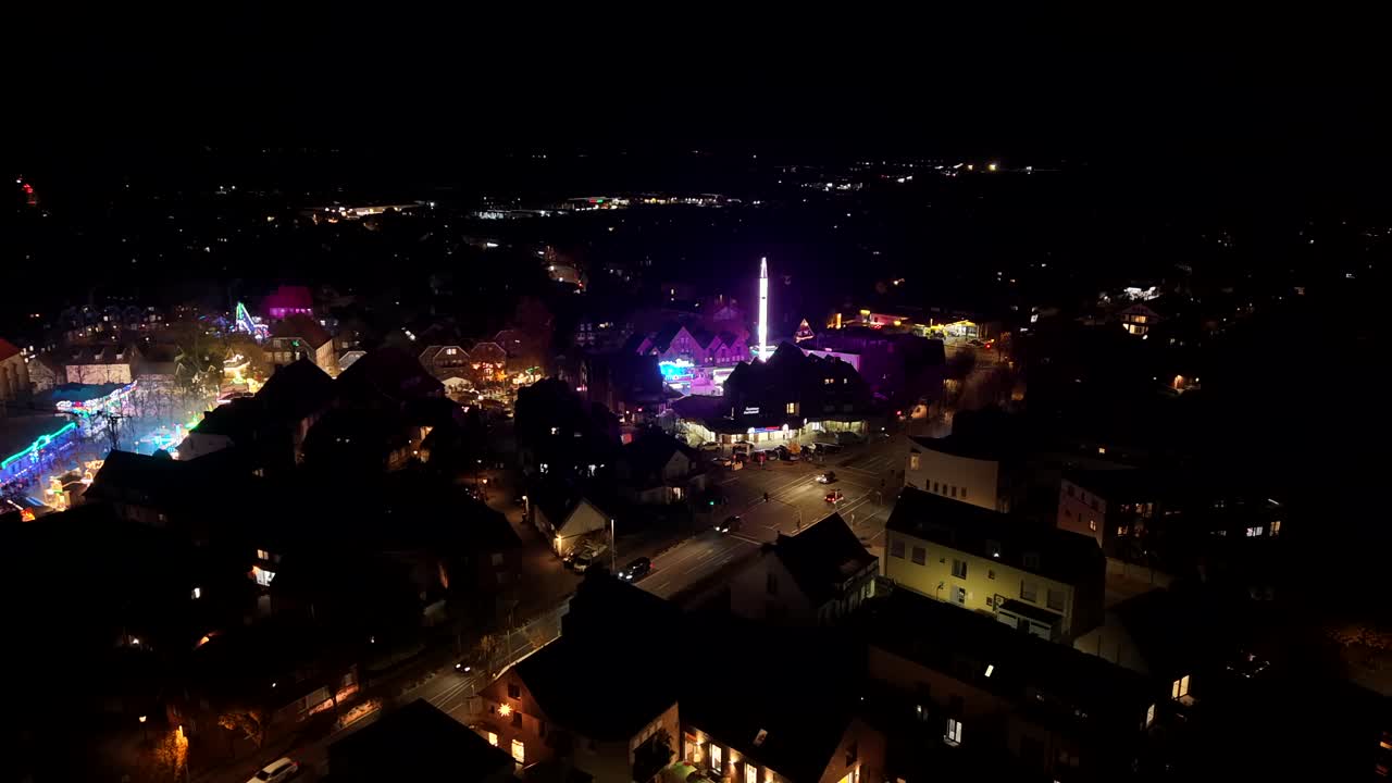 Carnival funfair event in american town with lighting tower and fairground rides. Driving cars on main street at night. Aerial flyover shot