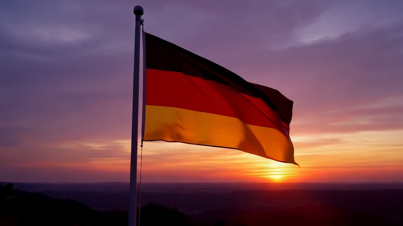Bandeira tricolor preta, vermelha e dourada tremulando em um mastro de metal, ondulando ao vento no topo de uma colina enquanto o sol se põe