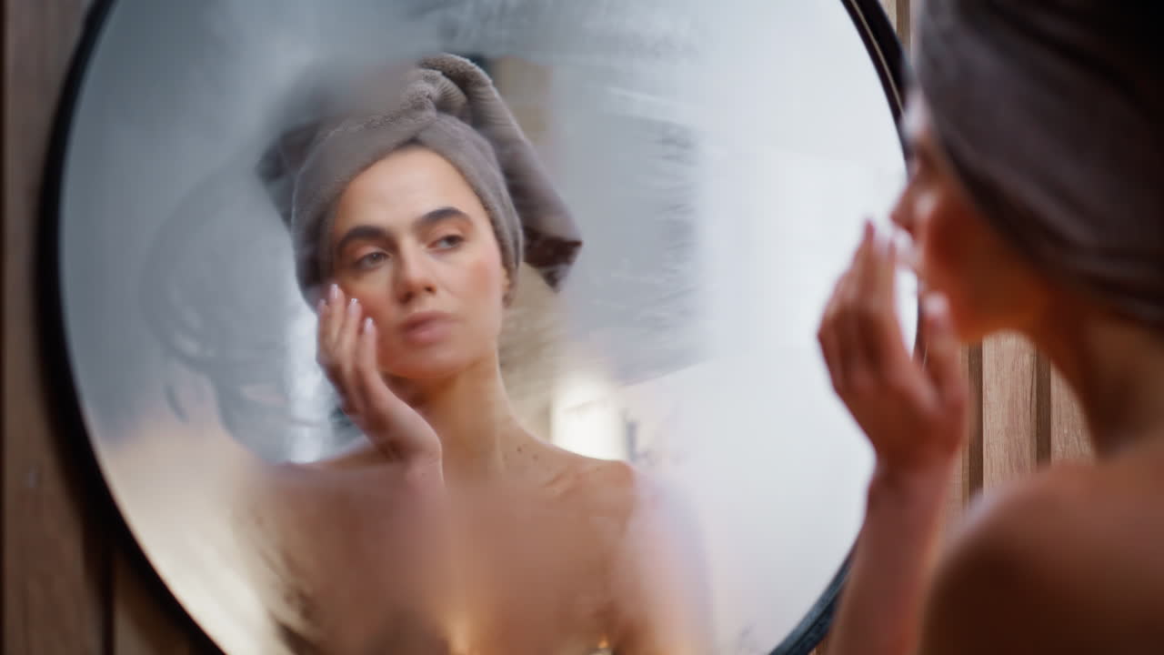 Primo piano di una modella che pulisce la superficie dello specchio del bagno. Giovane donna che si guarda allo specchio.