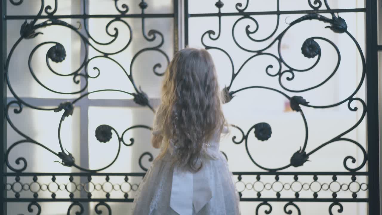 красивая девушка в праздничном платье закрывает кованую решетку дома