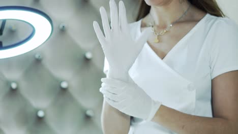 woman beautician in a white coat puts on white sterile gloves before the procedure of permanent makeup