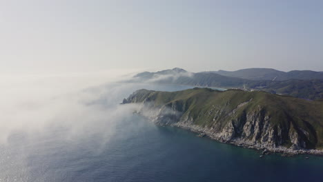 bird's eye view of a breathtaking steep rocky coast line with heavy dense fog approaching from the sea and moving over hill, far east, russia, sea of japan