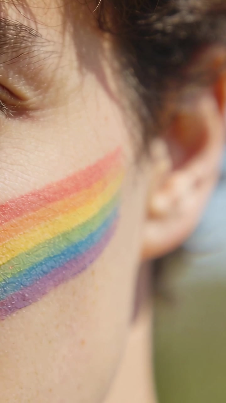 Vertical video: Squinting from sun glare, male teen turning outdoors, showing rainbow face paint