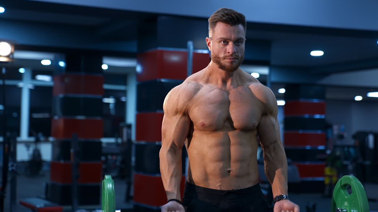 Handsome male athlete with perfect body trains with barbell in gym. Strong body and perfect abs. Slow motion.