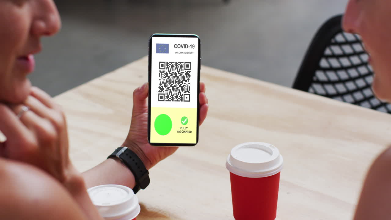 Man at cafe showing smartphone with covid vaccination certificate, eu flag and qr code on screen