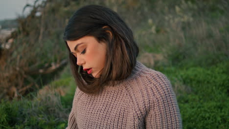 una mujer romántica sentada en la hierba con un suéter gris de cerca. una chica relajada en la naturaleza.