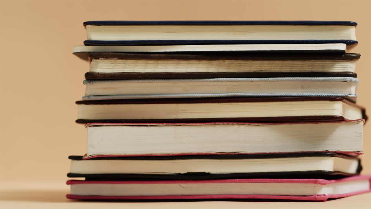 A stack of books with various covers sits against a beige background
