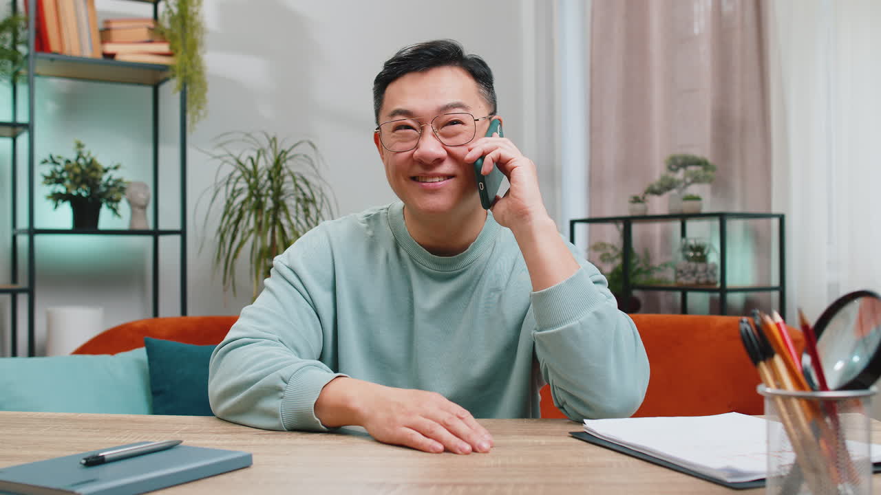 Happy excited asian man making phone conversation call with friends sitting on couch at home room