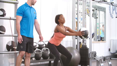 mujer joven haciendo agachadas en un gimnasio con el consejo de un entrenador