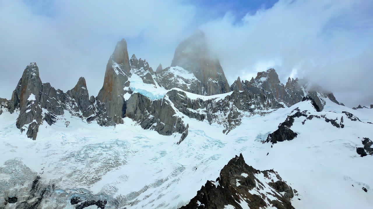 Aerial drone view of the dramatic granite peaks of Fitz Roy partially covered by clouds with glaciers stretching across the slopes