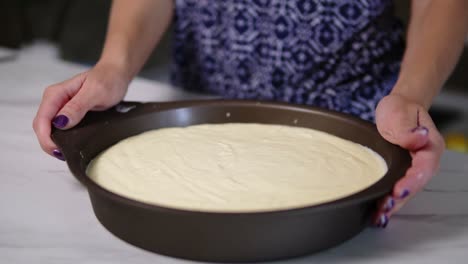 Close-Up-view-of-female-hands-shaking-baking-pan-with-white-cream-cheese-topping-spread-on-the-a-biscuit-base.-cheesecake