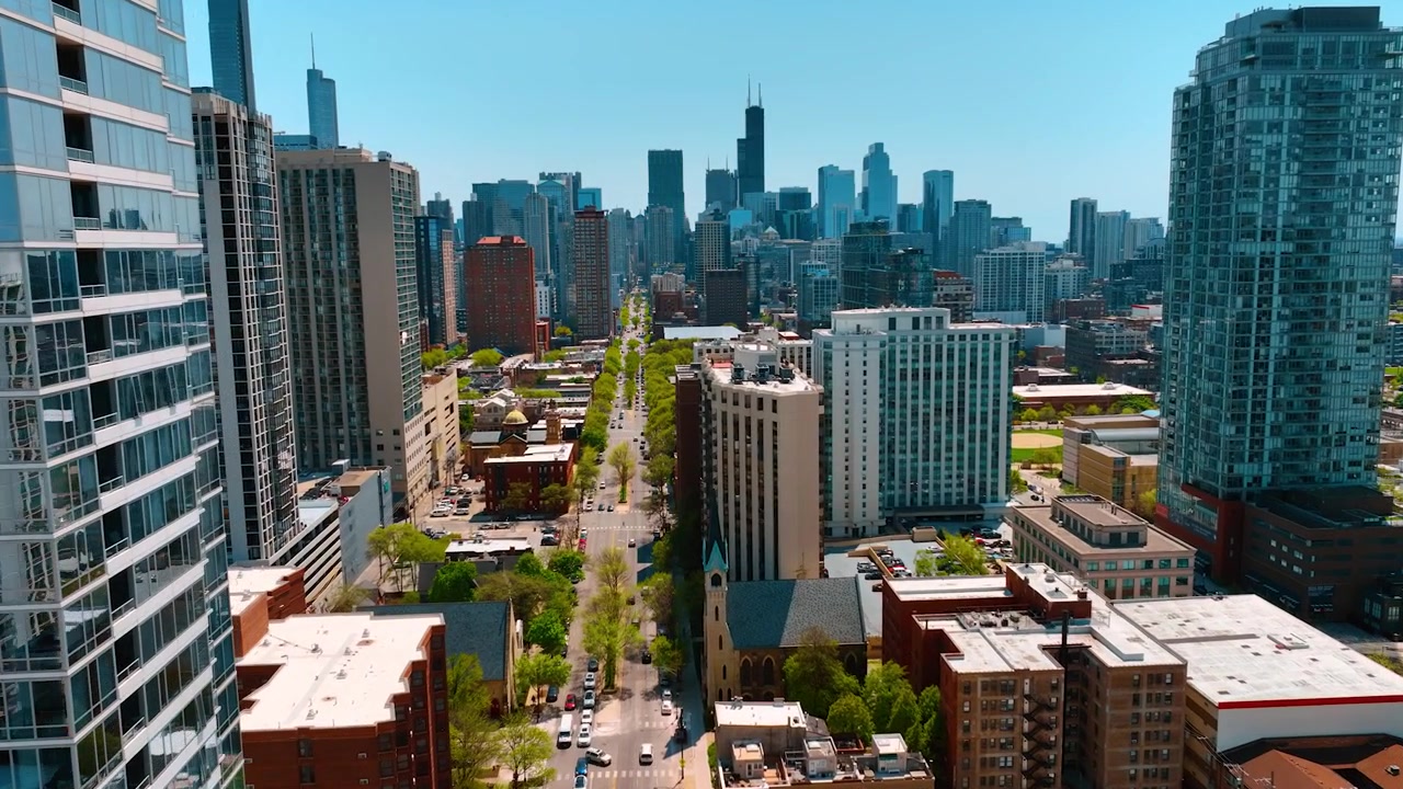 Long straight street with green trees growing along. Flight over the road leading to the downtown of Chicago, Illinois, USA.