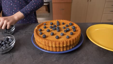 young girl is decorating a delicious blueberry cake in a kitchen