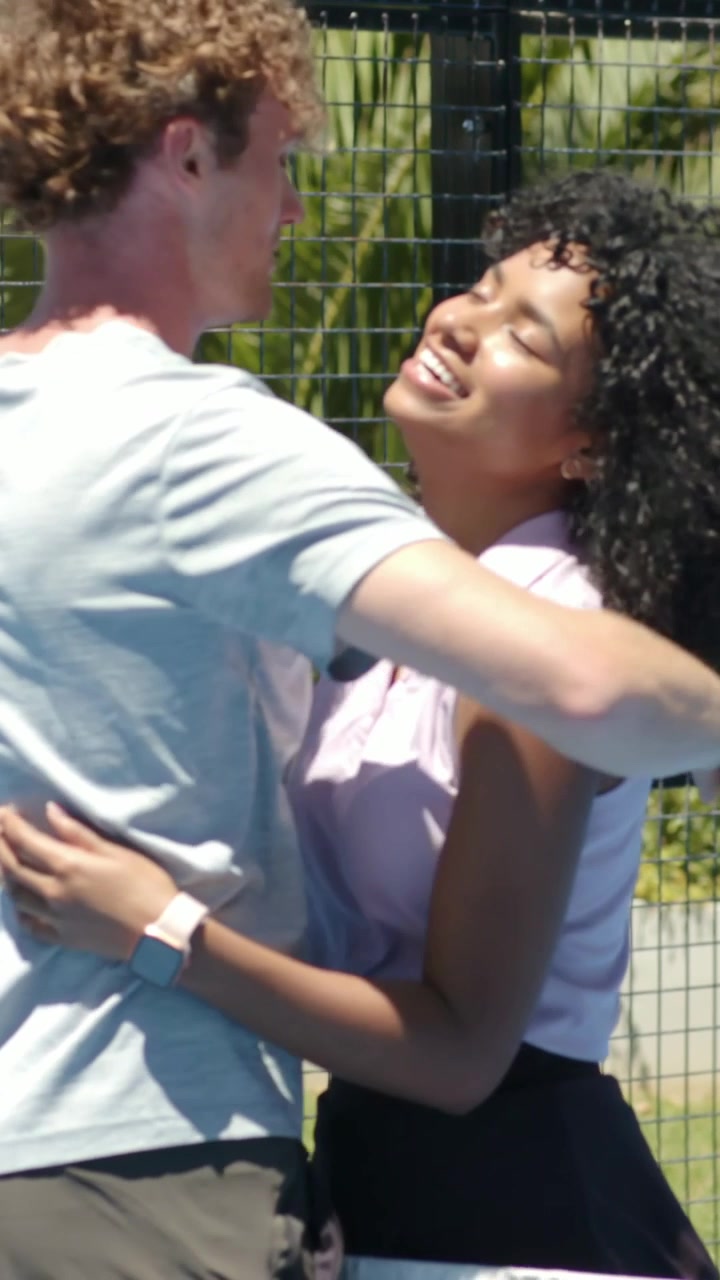 Video verticale: Uomo che si avvicina e abbraccia una donna in polo rosa su un campo da paddle mentre tiene la racchetta.