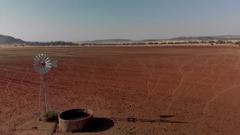 aerial dolly shot of a working windpump in red dry field with water in dam