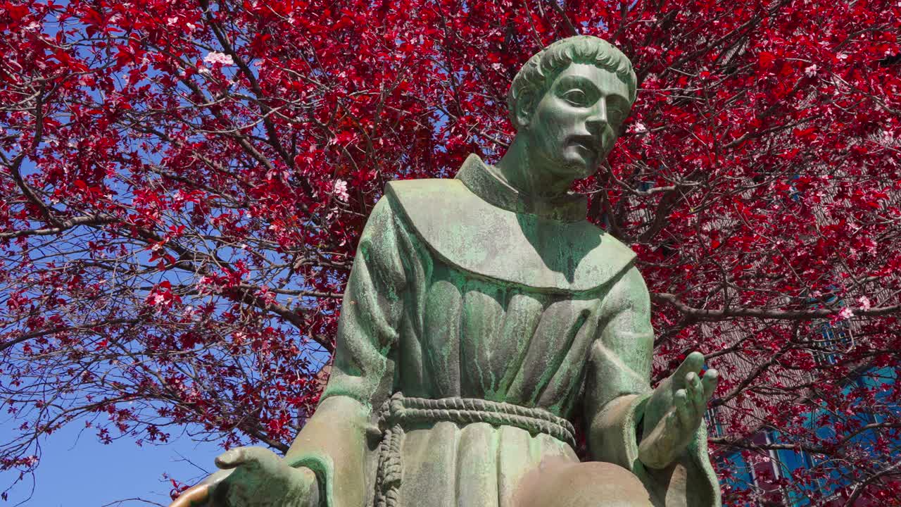 Low angle shot of a saint statue with water from a fountain reflecting on it and bright red leaves trees in the background in Milan Milano Italy