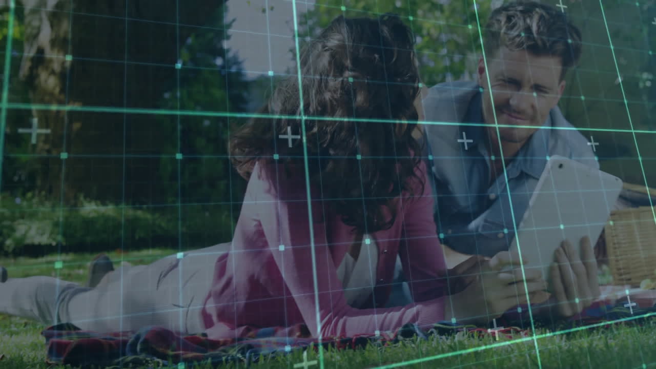 Couple lying on picnic blanket in park, viewing tablet technology with animated data charts