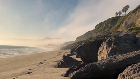 las olas del océano azul y verde de la playa brumosa de malibu de 4k chocan contra la costa rocosa en un día nublado b roll