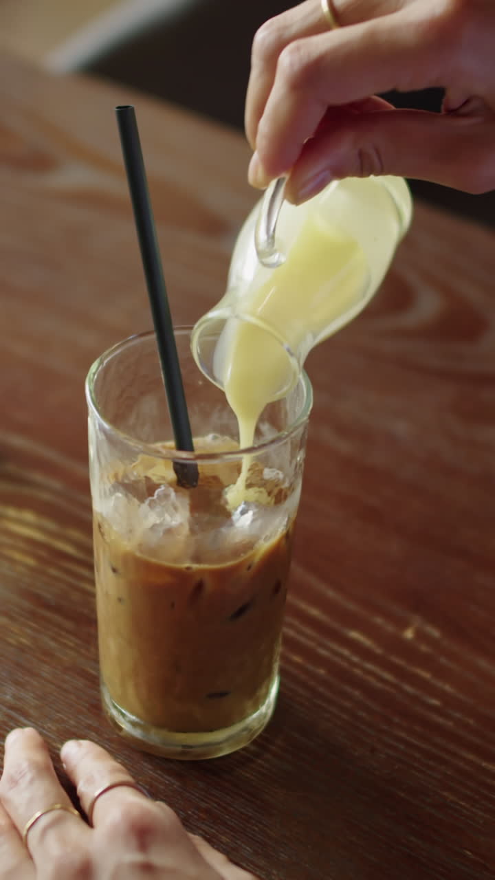 Hands of Person Adding Cream to Iced Coffee in Cafe
