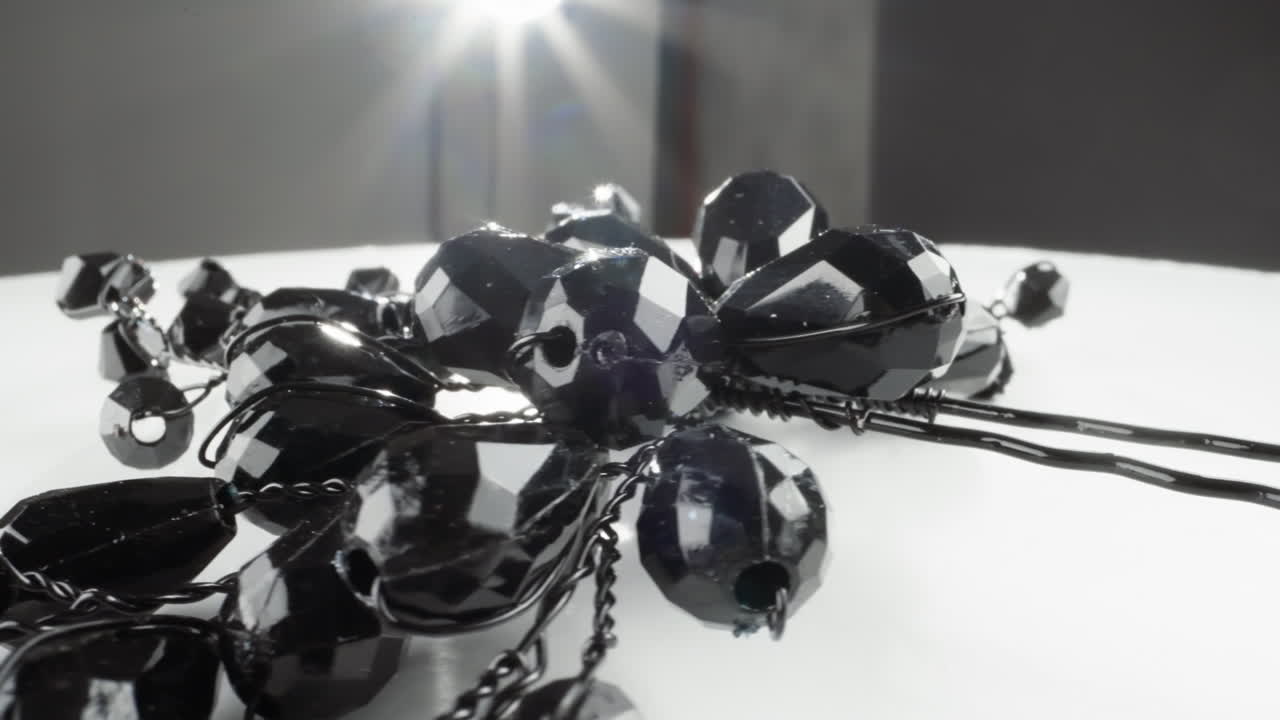 блестящие черные фасетные бусы ожерелья с световыми отражениями на белой поверхности