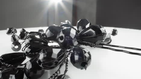 cuentas brillantes de facetas negras de un collar con reflejos de luz en la superficie blanca