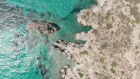 Overhead-Top-Down-Aerial-Flight-over-Greek-Island-Milos-Turquoise-Blue-Ocean-with-Rocky-Cliff-Coast