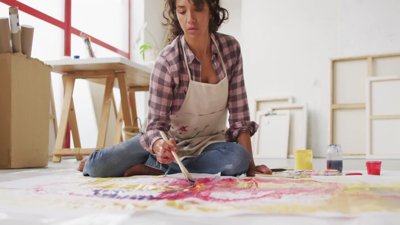 video de una artista femenina biracial pintando en el suelo en un estudio
