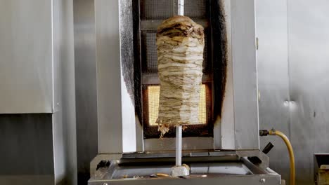 big chicken shawarma skewer hanged on grill turning around on fire