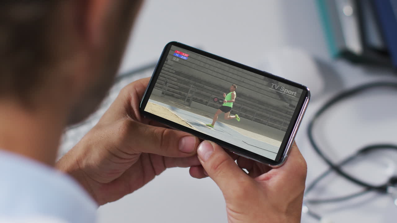 compuesto de un médico masculino viendo un evento de salto de longitud de atletismo en un smartphone