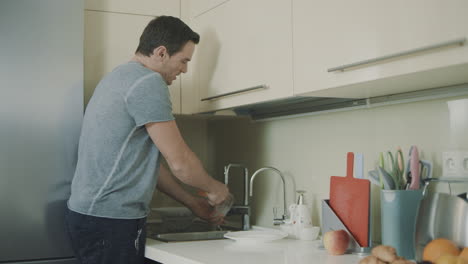 Cheerful-husband-doing-household-chores.-Smiling-person-washing-glass