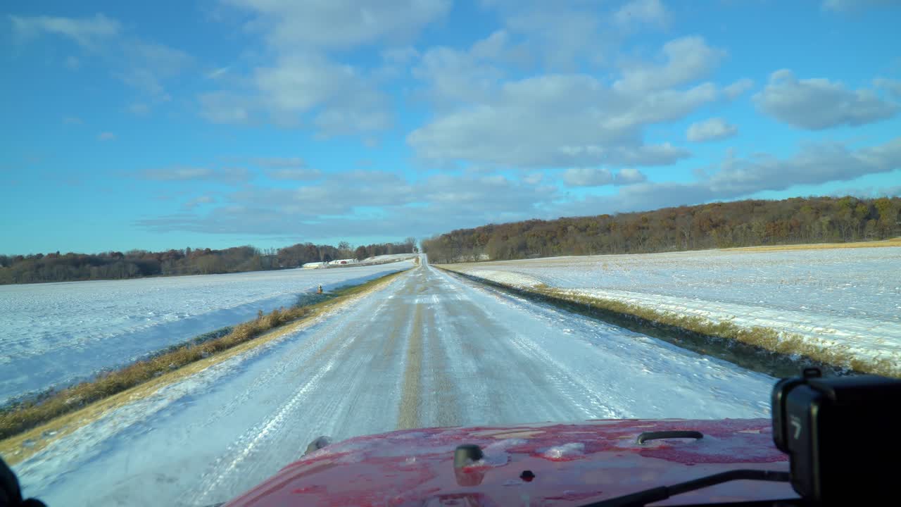 Driver POV on a snowy country road past empty fields on a sunny late autumn afternoon; driving a red sports utility vehicle SUV; point of view