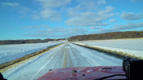 driver pov on a snowy country road past empty fields on a sunny late autumn afternoon; driving a red sports utility vehicle suv; point of view
