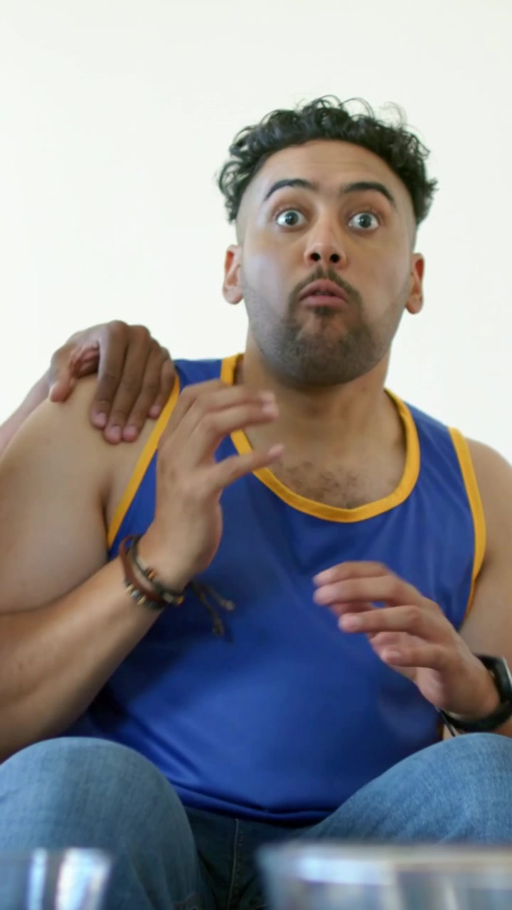 Vertical video: Reacting offscreen, man in jersey snacking, rising, being helped on couch, bowl