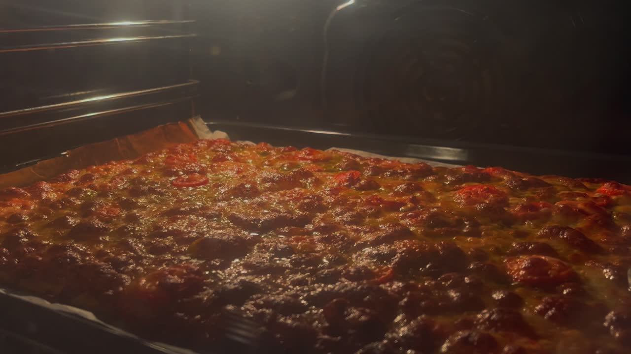 En herlig visning av en gyllen, boblende pizza som stekes i en ovn, fanget under varm belysning. Den perfekt stekte skorpen og smeltende osten er uimotståelig tiltalende