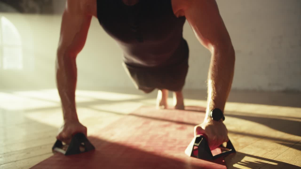 Close-up shot of a man in a black T-shirt doing push-ups using special handrests on a red mat