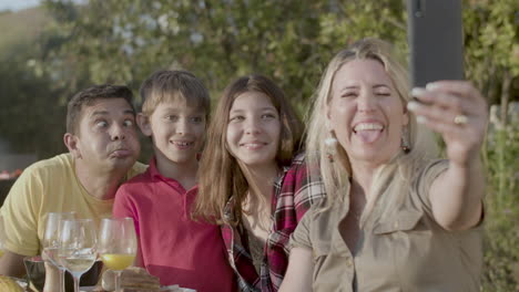 happy woman taking selfie of her grimacing family outdoors