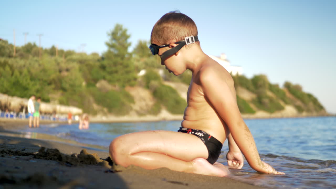 Child sitting on the sand and enjoying sea waves washing him